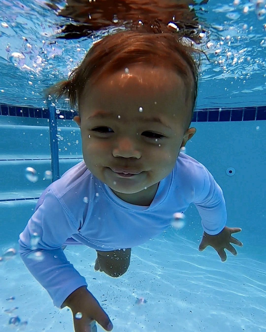 Baby in a lavender rash guard swimming underwater toward the camera during a CM SWIM CO survival swim lesson in Sacramento