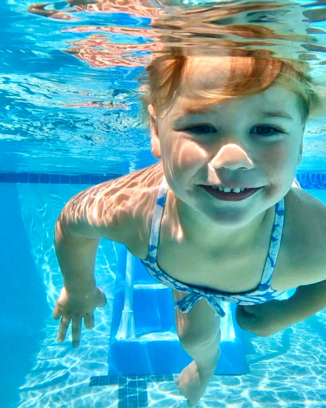 Smiling young girl swimming underwater during a CM SWIM CO survival swim lesson